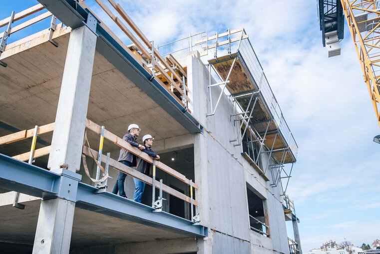 Zwei Leyrer + Graf Mitarbeiter stehen erhöht auf einer Baustelle und besprechen das weiter Vorgehen auf der Baustelle